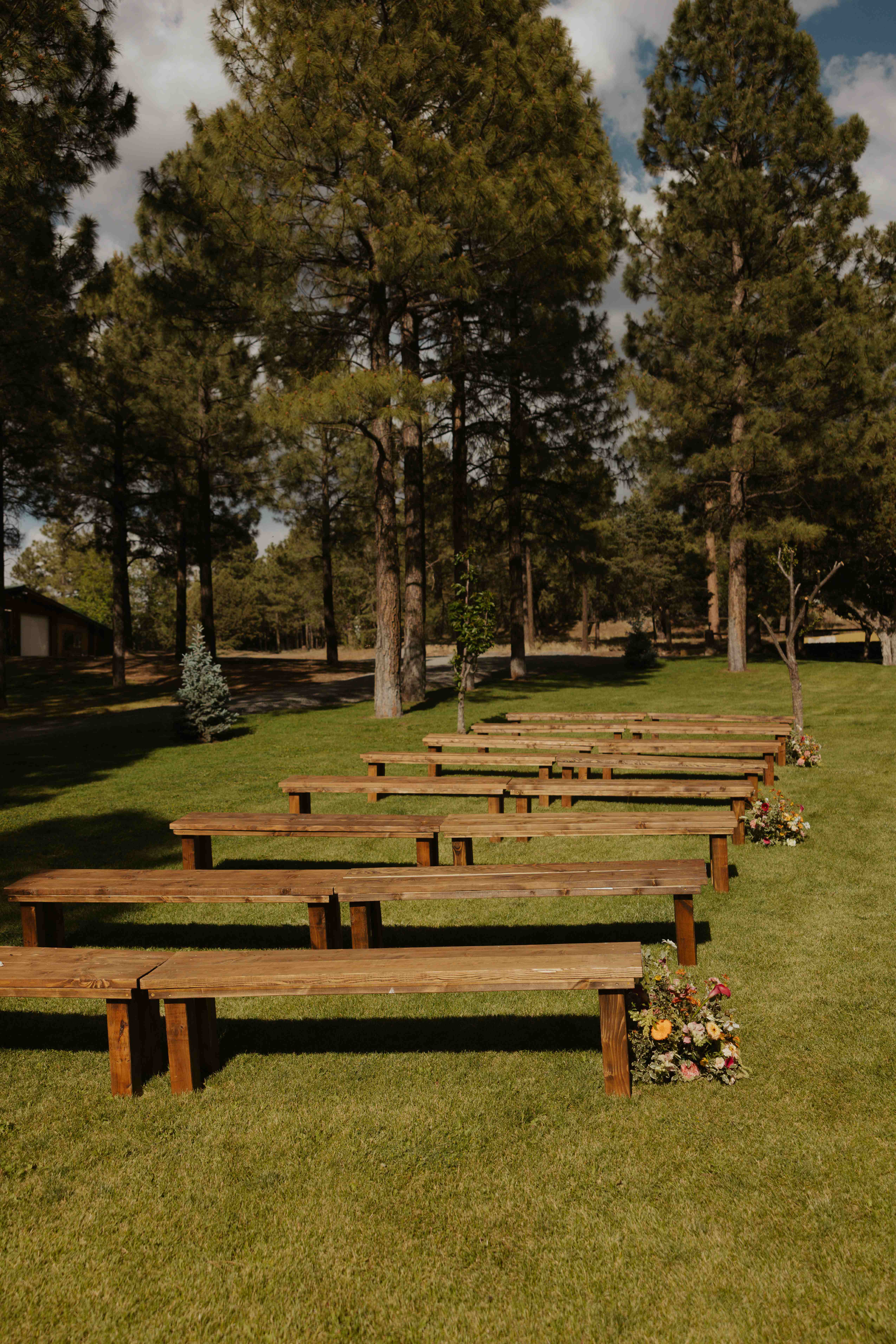 Rows of wooden benches with wildflower arrangements lining the aisle on a grassy lawn among tall Ponderosa pines