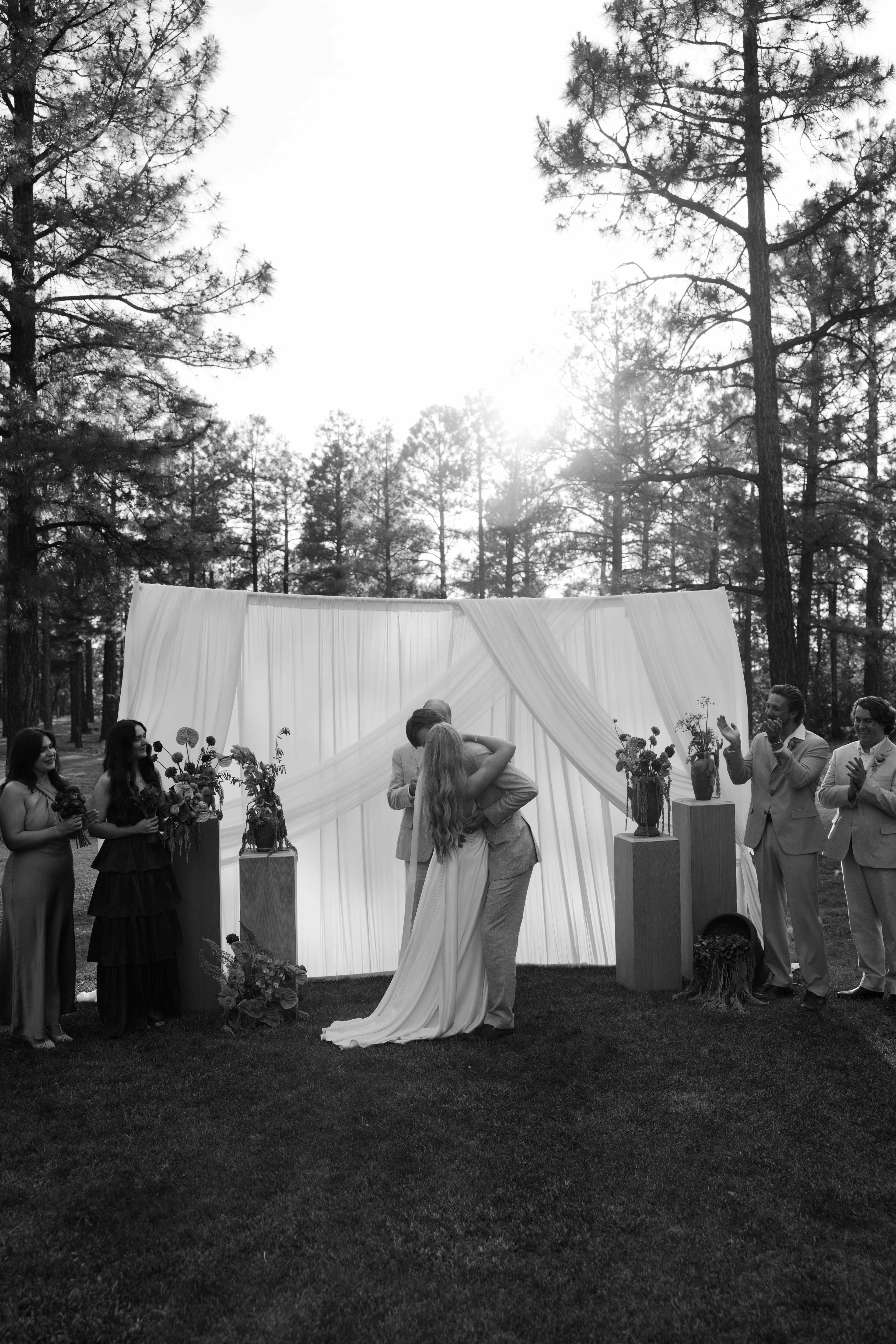 Black-and-white photo of the couple embracing at the altar as the wedding party applauds