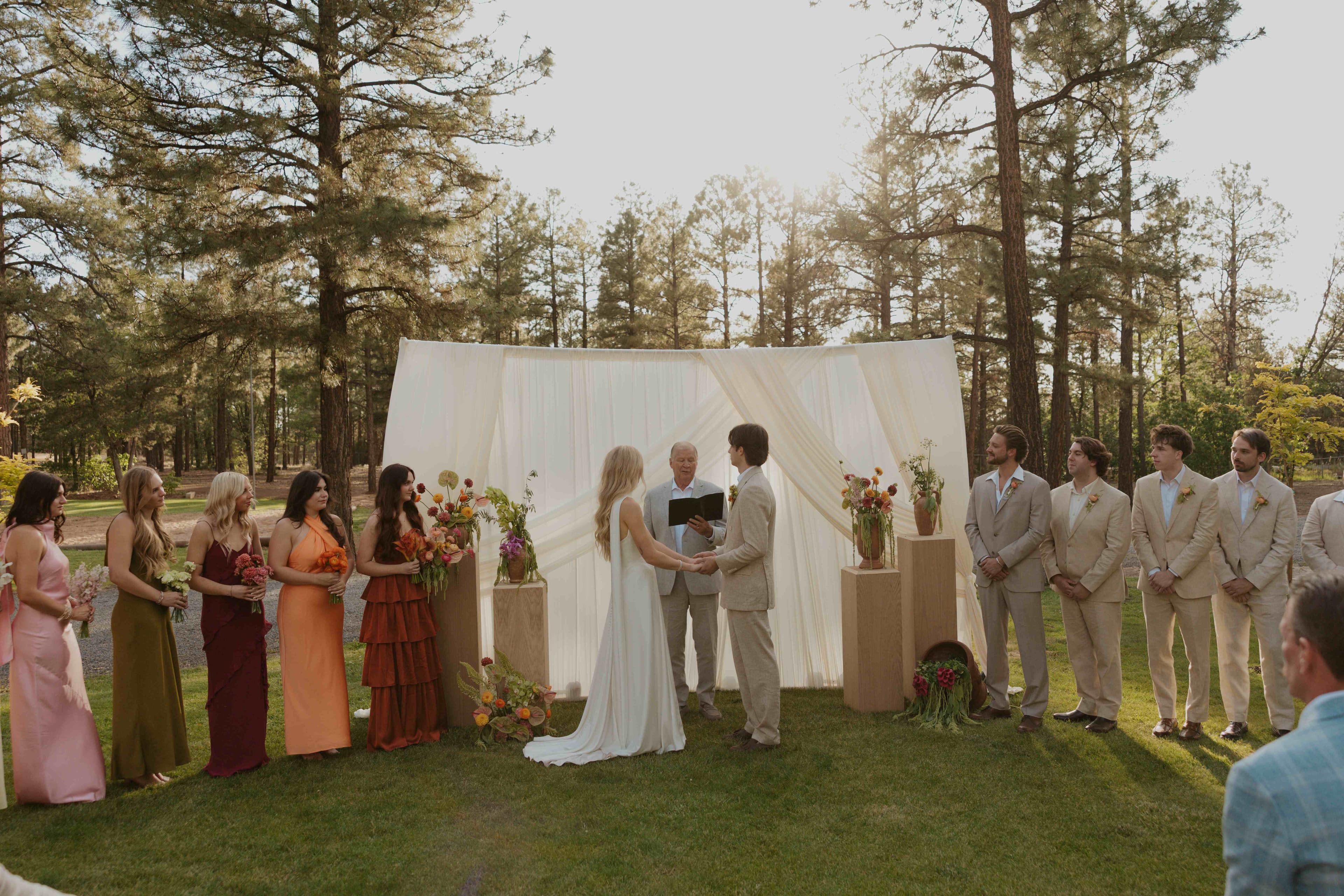 Bride and groom holding hands at the altar as the officiant reads, wedding party lined up beside them