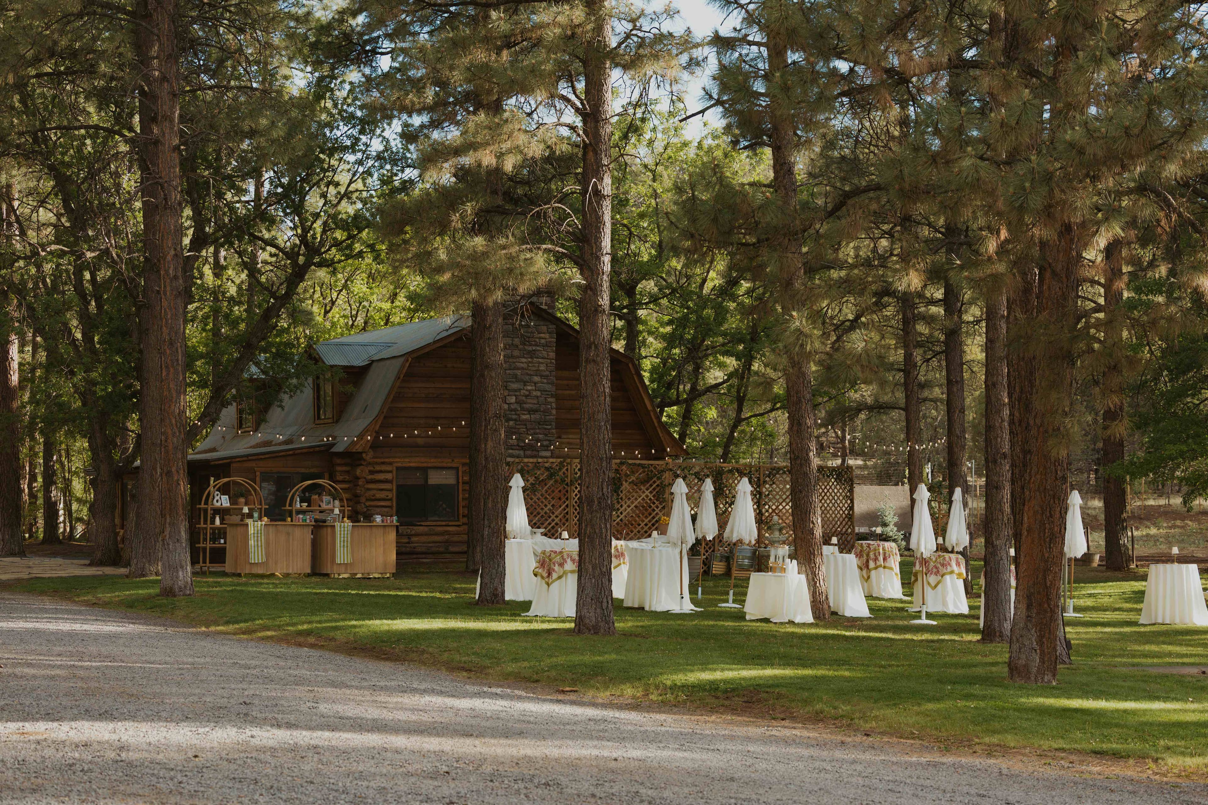 Wide establishing shot of the log cabin, bar, and umbrella-dotted cocktail area among the Ponderosa pines