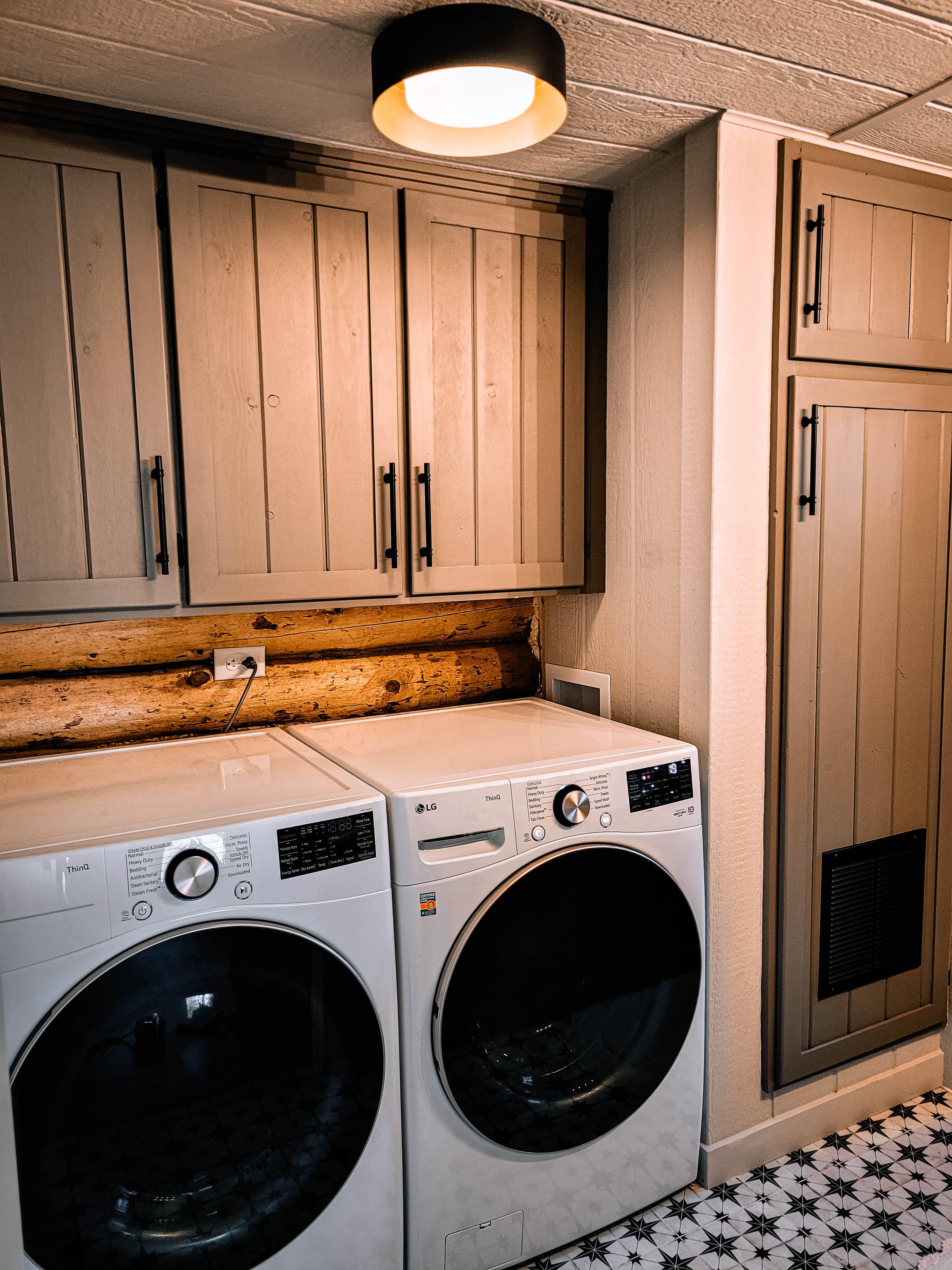 Cabin laundry room with LG front-load washer and dryer, custom wood cabinetry, and star-pattern tile floor
