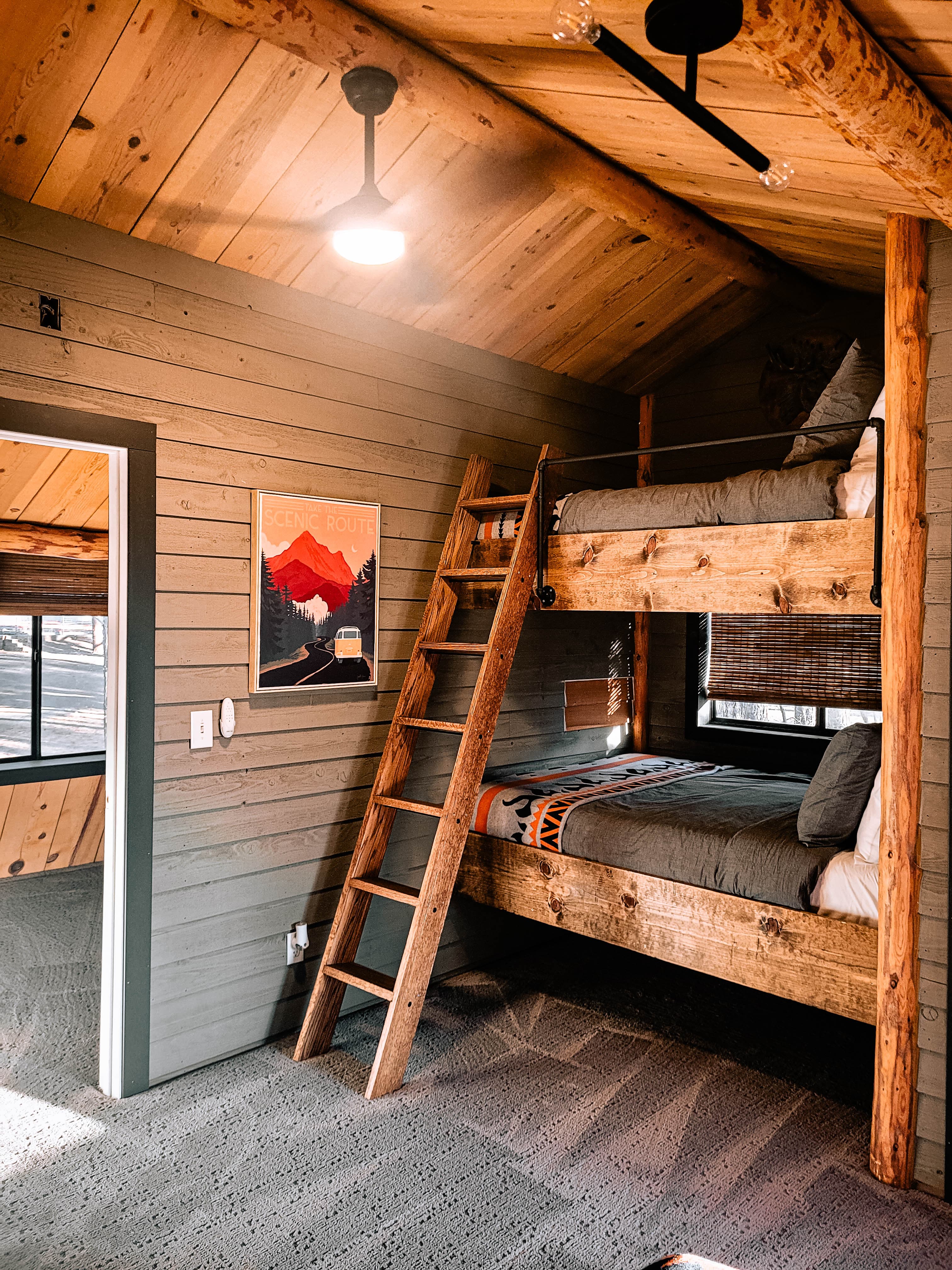 Second bunk room view showing bunk bed ladder, log post, and en-suite bathroom doorway with striped shower curtain
