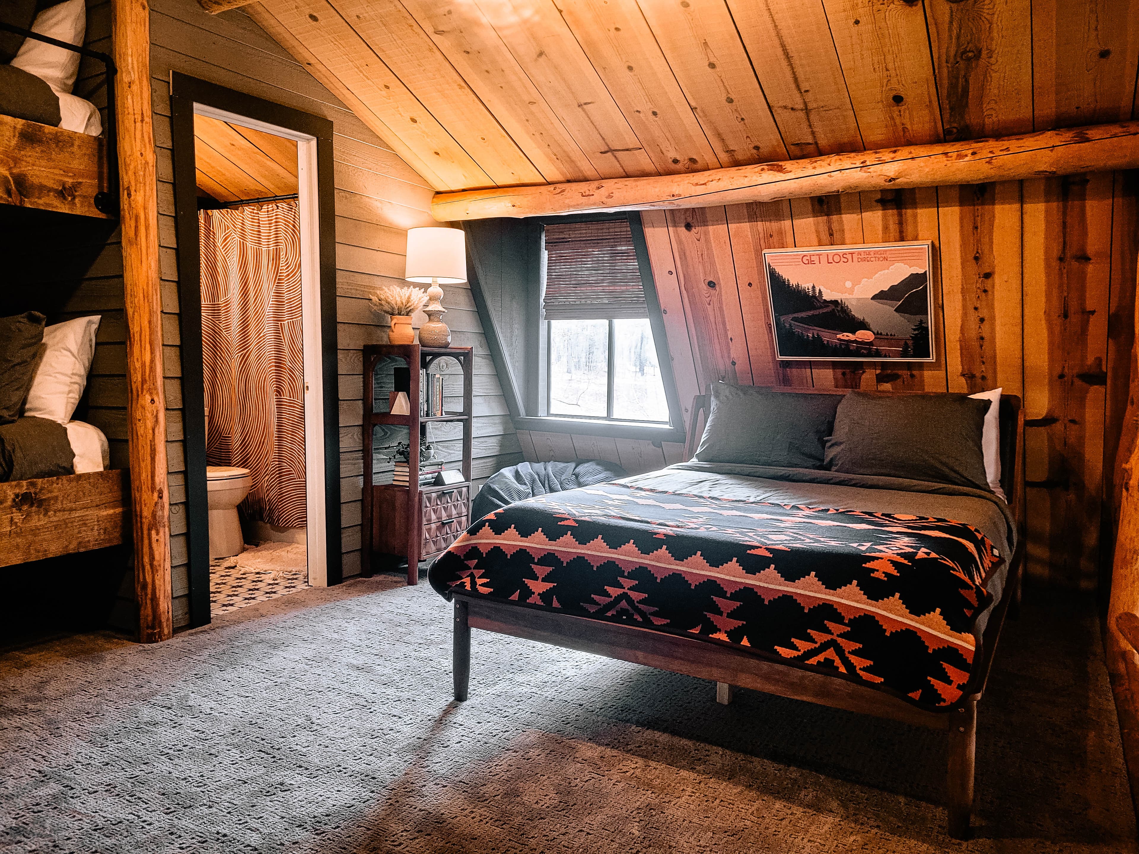 Cabin loft bedroom with queen bed, Pendleton blanket, national park posters, and slanted wood ceiling