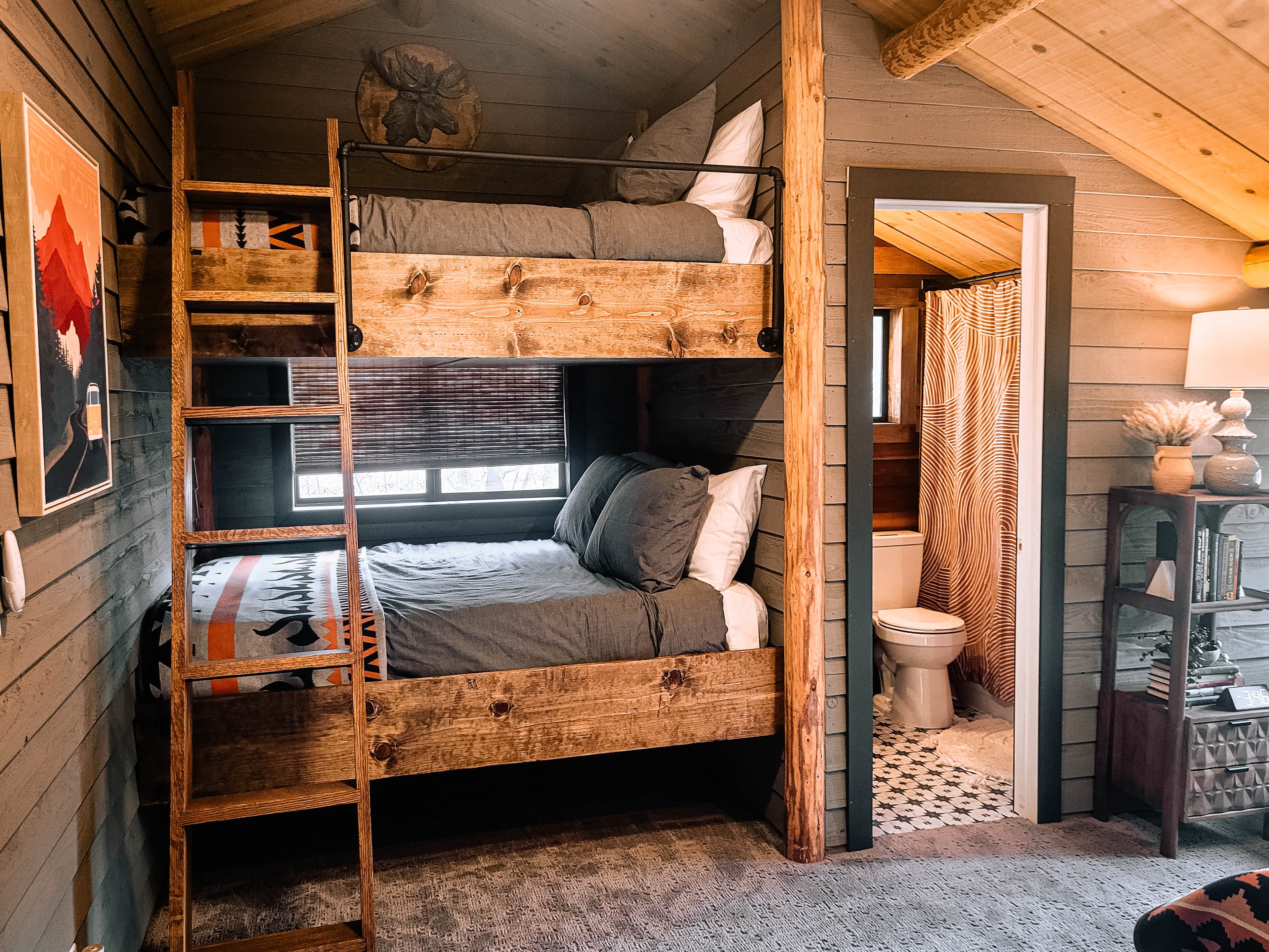 Cabin bunk room with rustic built-in bunk beds, log post, ladder, dark shiplap walls, and Scenic Route poster