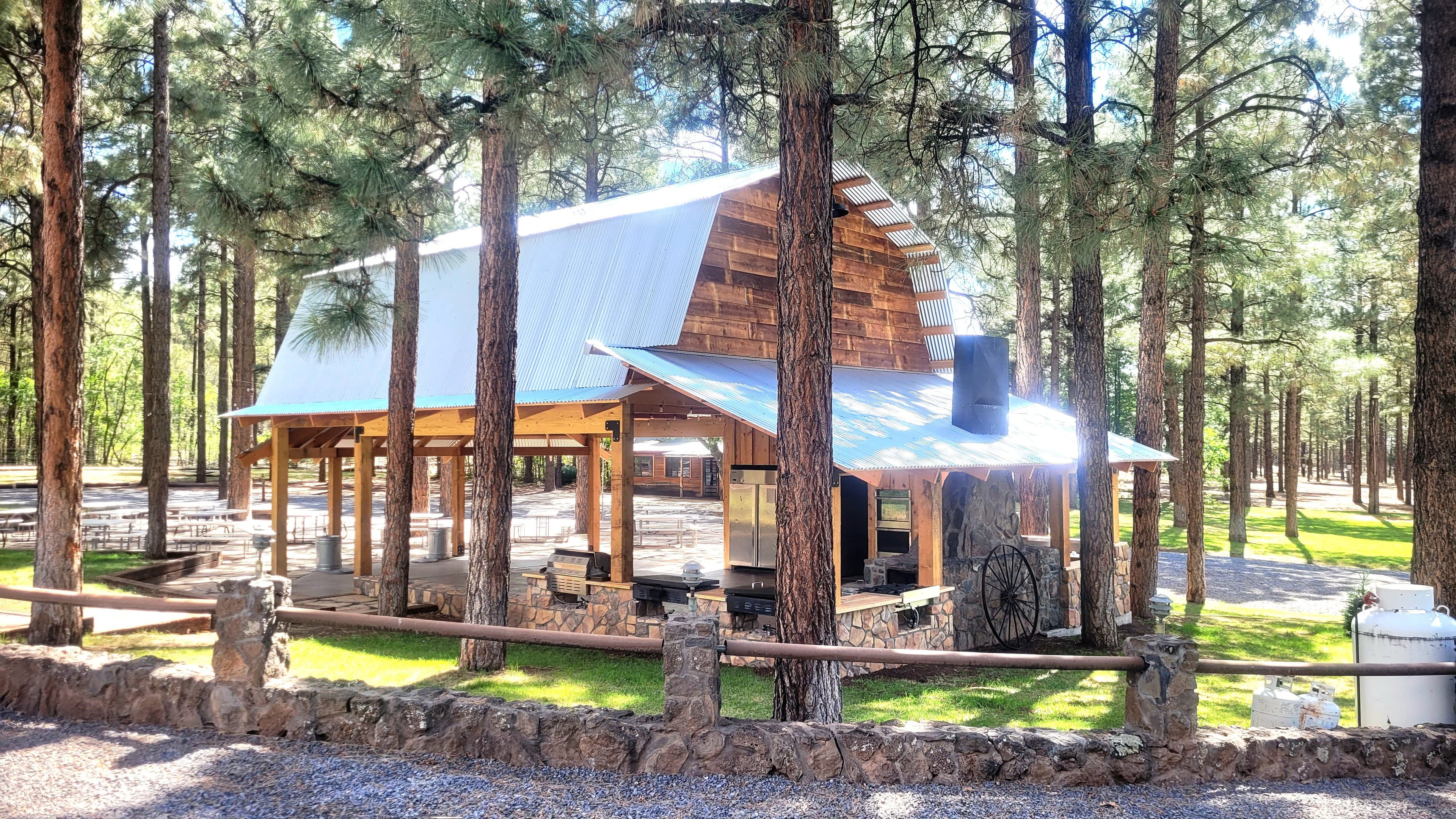 Ramada kitchen and cooking station with stone masonry base, corrugated metal roof, and wagon wheel accent
