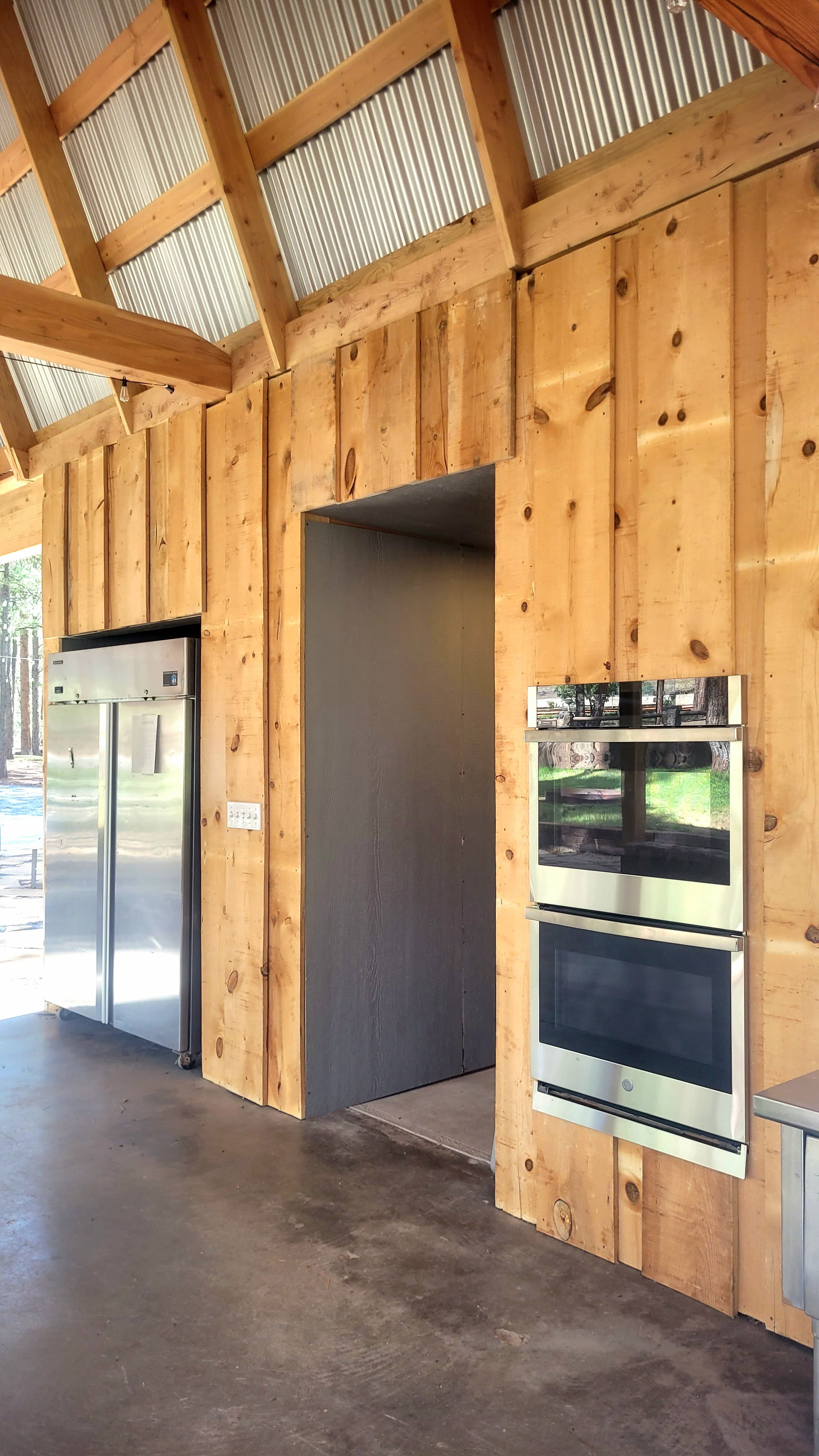 Inside the ramada kitchen with wood-paneled walls, commercial stainless refrigerator, central doorway, and double wall oven